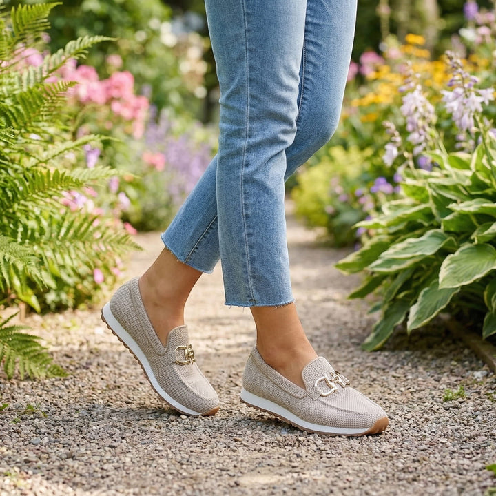 Nora & Elise Susie beige orthopaedic moccasin trainers with gold horseshoe detail and white sole, worn with jeans.